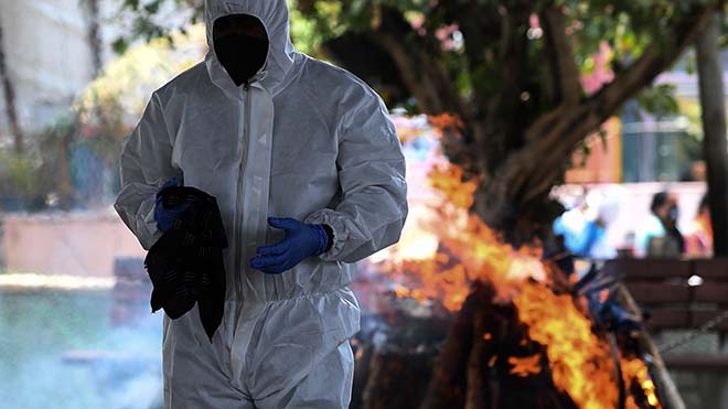 يقف شخص بمعدات الوقاية الشخصية أمام محرقة حرق جثة شخص توفي بسبب الفيروس التاجي